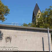 Kölnischer Kunstverein Der Kölnische Kunstverein: Moderne Betonarchitektur vor einem Kirchturmhintergrund, von Bäumen umrahmt.The Kölnischer Kunstverein: Modern concrete architecture in front of a church tower background, framed by trees.
