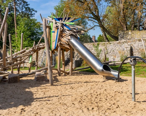Drachenspielplatz Ratingen Ein Abenteuerspielplatz mit Holzstruktur und Rutsche lädt in einer naturnahen Umgebung zum Spielen ein.