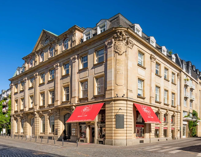 Farina Fragrance Museum Das Farina-Haus in Köln zeigt eine historische Fassade mit klassischer Architektur und rot-weißen Markisen vor einem klaren blauen Himmel.The Farina House in Cologne features a historic façade with classic architecture and red and white awnings against a clear blue sky.