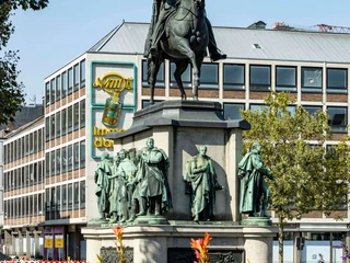 Equestrian statue of King Frederick William III. Reiterstandbild von König Friedrich Wilhelm III. auf einem Sockel, umgeben von vier stehenden Figuren. Eventuell im Hintergrund Gebäude und Bäume zu sehen.Equestrian statue of King Frederick William III on a pedestal, surrounded by four standing figures. There may be buildings and trees in the background.