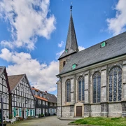 Historischer Ortskern mit Kirchplatz in Wülfrath Kirchplatz in Wülfrath mit beeindruckender Kirche und traditionellen Fachwerkhäusern unter blauem Himmel.
