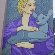 Mural Eine Wandmalerei zeigt eine Frau mit blonden Haaren, die in einer lila Jacke ein Reh hält. Dies ist ein Werk des Künstlers El Bocho, das an einer Hausfassade in Köln zu bewundern ist.A mural shows a woman with blonde hair holding a deer in a purple jacket. This is a work by the artist El Bocho, which can be admired on the façade of a house in Cologne.
