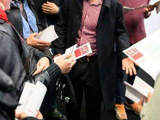 ART COLOGNE Gruppe von Menschen hält Flugblätter mit "ART COLOGNE"-Logo und diskutiert angeregt.Group of people holding leaflets with the "ART COLOGNE" logo and having a lively discussion.