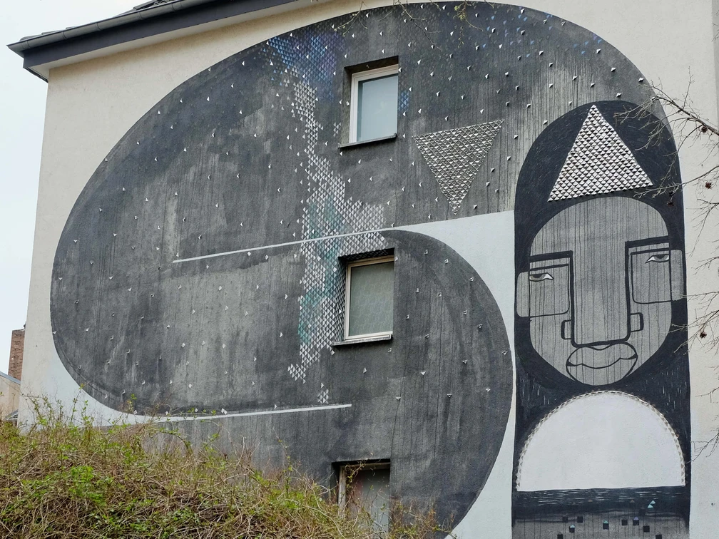 Mural Das beeindruckende Wandgemälde auf dem Gebäude zeigt abstrahierte Formen und Gesichter in Schwarz-Weiß-Tönen.The impressive mural on the building shows abstract shapes and faces in black and white tones.