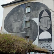 Mural Das beeindruckende Wandgemälde auf dem Gebäude zeigt abstrahierte Formen und Gesichter in Schwarz-Weiß-Tönen.The impressive mural on the building shows abstract shapes and faces in black and white tones.