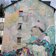 Mural Barrierefreie Beschreibung: Eine farbenfrohe Wandmalerei zeigt einen schlafenden Sufi mit Flügeln, umgeben von bunten Elementen.Accessible description: A colorful mural shows a sleeping Sufi with wings, surrounded by colorful elements.