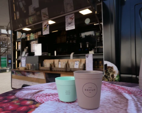 Sheka Forest Kaffee Recup Ein brauner und ein grüner Pfandbecher der Marke Recup stehen vor dem Kaffeemobil auf einem Tisch
