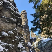 Bielatal Felsige Schlucht mit schneebedeckten Formationen und hohen Kiefern unter klarem, blauem Himmel.