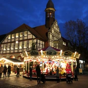 Adventszauber Nienburg (2).jpg Weihnachtlich beleuchteter Marktplatz in Nienburg mit Karussell und Fachwerkgebäude bei Dämmerung.