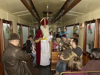 Nikolaus_Selfkantbahn2.jpg Nikolaus in einem nostalgischen Eisenbahnwaggon, umgeben von fröhlichen Menschen.