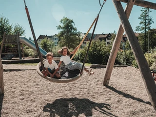 Zwei Kinder sitzen in einer Korbschaukel auf dem Mehrgenerationen-Spielplatz Schelklewiesen