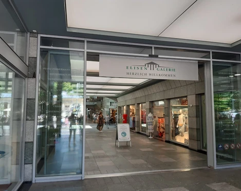Eingang zu ElisenGalerie mit gläsernen Automatik-Türen und einem Schild, auf dem "ElisenGalerie" steht und das Logo der ElisenGalerie.