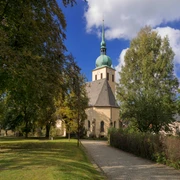 Park with Peter-Paul Lutheran Church Eine Kirche mit grünem Turm steht zwischen Bäumen unter blauem Himmel; ein gepflasterter Weg führt dorthin.