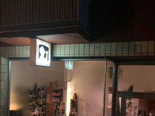 La Vincaillerie Abendliche Szene eines kleinen Weinladens mit beleuchteten Schaufenstern und vielen Weinflaschen.Evening scene of a small wine store with illuminated shop windows and many bottles of wine.