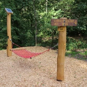 Hängematte Rote Hängematte aus robustem Material im Wald, flankiert von Holzstangen und Wegweiser "Literarischer Weg".