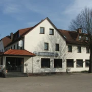 Hörster Krug Ein traditionelles Fachwerkgebäude mit roten Ziegeldächern und weißen Wänden, umgeben von Bäumen.