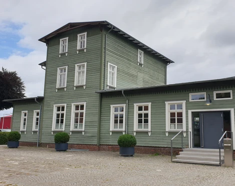Historischer Bahnhof Rahden mit grüner Holzfassade und symmetrischen weißen Fenstern.