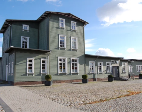 Historisches Bahnhofsgebäude aus Holz mit grüner Fassade und weißen Fenstern im Sonnenschein.