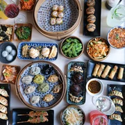 WeiundWei.jpg Tisch mit verschiedenen Asiatischen Spezialitäten wie Frühlingsrollen und Dumplings in unterschiedlichen Schalen, Tellern, Tabletts, Körben und Schüsseln.