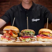 Champions Sports Bar - Gastronomie in Leipzig Ein Koch hält ein Holzbrett, auf dem drei Burger liegen
