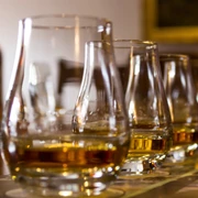 Bier- und Whiskey-Tasting.jpg Eine Reihe von Whiskeygläsern auf einem Tisch, im Hintergrund unscharfe Whiskeyflaschen.