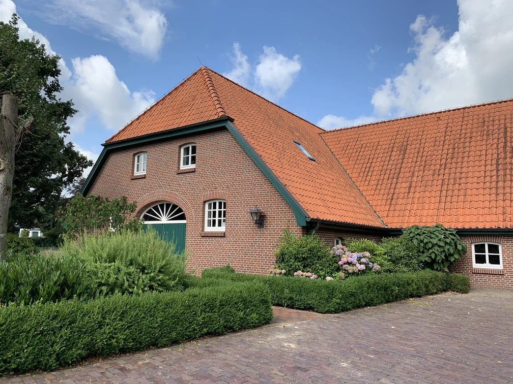img_0566 Ein traditionelles Backsteinhaus mit roten Dachziegeln, umgeben von grünen Pflanzen im Vordergrund.