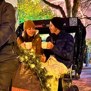 Rikolonia Köln Glühweinfahrt.png Zwei Personen sitzen am Abend hinten in einer Rikscha und trinken GlühweinTwo people sit in the back of a rickshaw in the evening and drink mulled wine