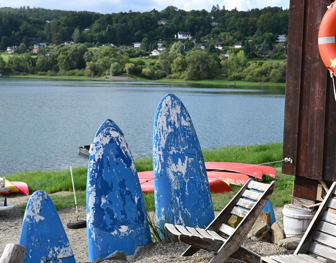 Stühle und ehemalige Surfbretter im Vordergrund und Edersee im Hintergrunf
