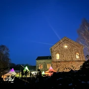 Ein historisches Backsteingebäude beleuchtet den Nachthimmel; bunte Lichter im Vordergrund.