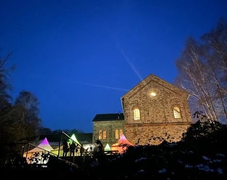 Ein historisches Backsteingebäude beleuchtet den Nachthimmel; bunte Lichter im Vordergrund.