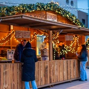 Sülzer Weihnachtsdorf Ein beleuchteter Weihnachtsmarktstand mit Personen und dekorativen Lichtern.An illuminated Christmas market stall with people and decorative lights.