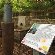 Rastplatz Riechen am Weg für Genießer - Urheber Stadt Werther.JPG Duftstation im Wald mit Infotafel und Zerstäuber, umrahmt von einer Steinmauer, herbstliche Blätter am Boden.