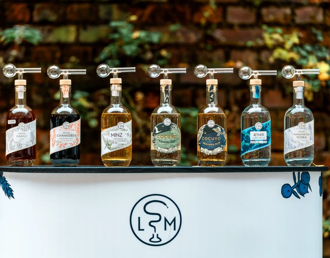 Produktvielfalt der Leipziger Spirituosen Manufaktur - Regionale Produkte aus Leipzig Aufgreit auf einem kleinen Tresen mit dem Logo der Leipziger Spirituosen Manufaktur stehen alle erhältlichen Produkte der Marke