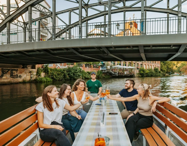 Bootstour auf der Weißen Elster - Wasserstadt Leipzig Eine Gruppe fährt mit einem Boot des Stadthafens Leipzig entlang der Weißen Elster, unter der Könneritzbrücke hindurch und stößt dabei mit einem erfrischenden Cocktail an, Wasserstadt Leipzig