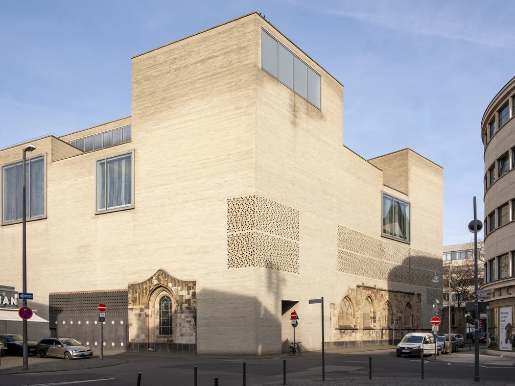 Das Kolumba Museum in Köln vereint moderne Architektur mit historischen Elementen. Die hellen Steinwände und großen Glasfenster des Gebäudes strahlen eine schlichte Eleganz aus.The Kolumba Museum in Cologne combines modern architecture with historical elements. The building's light-coloured stone walls and large glass windows radiate a simple elegance.