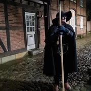 Nachtwächter Ein Nachtwächter in historischem Gewand mit Laterne steht auf einem Kopfsteinpflaster vor Fachwerkhäusern.