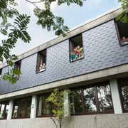Jugendherberge Lindlar Moderne Schulgebäude-Fassade mit Kindern, die aus den geöffneten Fenstern im oberen Stockwerk schauen.