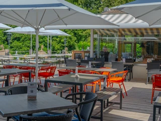 Terrasse Terrasse mit Holzboden, Esstischen, aufgespannten Schirmen und Blick ins Grüne.Terrace with wooden floor, dining tables, stretched umbrellas and a view of the greenery.