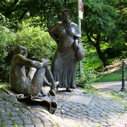 Lousberg Aachen Eine Marktfrau als Bronzefigur steht neben einer sitzenden Bronzefigur, die den Teufel darstellt.