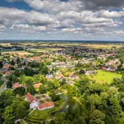 Luftaufnahme des Kurparks Bad Holzhausen mit grünen Wiesen, einem Teich und umliegenden Gebäuden.