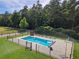 Ponyhof Hagedorn Ein Außenpool auf einer gepflasterten Fläche, umgeben von grüner Wiese und dichten Bäumen.
