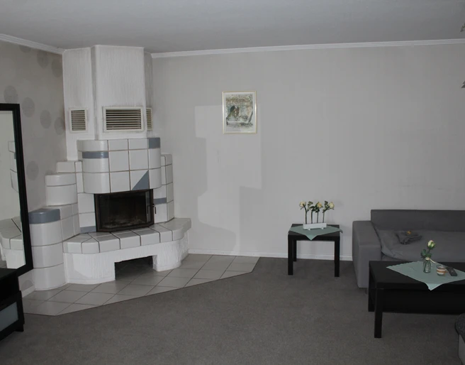 Stellmanns Gästehof Wohnraum mit modernem Kaminofen, grauem Ecksofa, Couchtisch und dezent dekorierten Wänden.