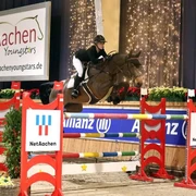 Eine Reiterin springt mit einem Pferd über ein Hindernis in einer weihnachtlich geschmückten Reithalle.A rider jumps over an obstacle with a horse in an indoor riding arena decorated for Christmas.Une cavalière saute un obstacle avec son cheval dans un manège décoré pour Noël.Een ruiter springt met een paard over een hindernis in een overdekte rijhal die versierd is voor Kerstmis.