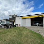 Flugplatz mit Hangars und einer gelben Markierung "Nienburg", Wiese im Vordergrund.