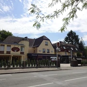 Außenansicht vom Hotel im Park, Haan Das Bild zeigt die Außenansicht eines Hotels mit braunem Dach und mehreren Stockwerken in einer städtischen Umgebung, umgeben von Bäumen und einer Straße im Vordergrund.