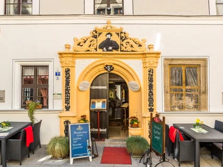 Romantik Hotel Deutsches Haus entrance portal Eingang eines historischen Gebäudes mit gelbem Torbogen, dekorativen Elementen und Schildern, umgeben von Tischen mit roten Decken und Blumen.