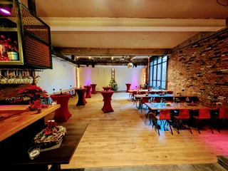 La Fabrik (3) Innenraum mit großen Tischen an der rechten Wand und mehreren Stehtischen in der Mitte. Links ist eine Bartheke.