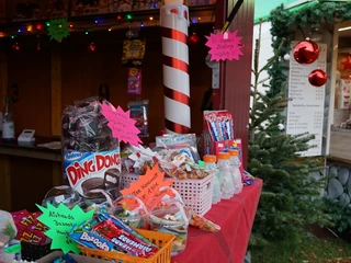 Süßes im Winter Verkaufsstand mit Süßwaren, festlicher Dekoration, Lichterkette und Weihnachtsbaum im Hintergrund.