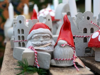 Kleine Weihnachtsfiguren Weihnachtliche Figuren aus Beton mit roten Mützen und Pilzen, festlich auf einem Holztisch arrangiert.