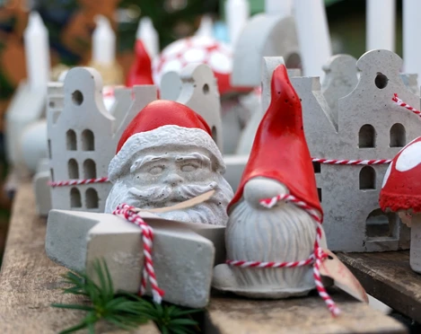 Kleine Weihnachtsfiguren Weihnachtliche Figuren aus Beton mit roten Mützen und Pilzen, festlich auf einem Holztisch arrangiert.